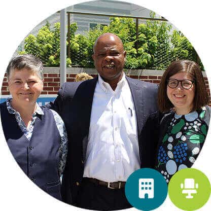 Three adults, two women and one man in a suit, smile outside for a photo. Trees and a building—reflecting Affordable Homes & Communities—form the backdrop. Two icons are overlaid at the bottom.