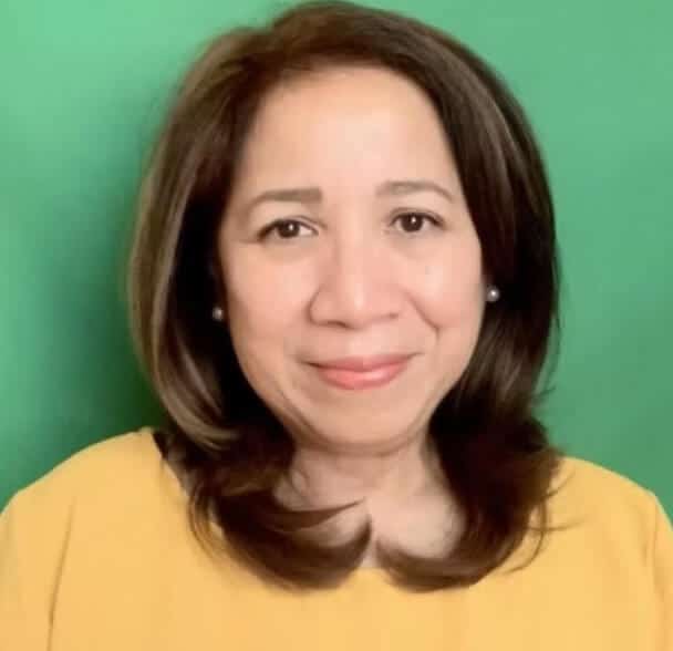 A woman with shoulder-length brown hair, wearing a yellow top, smiles softly in front of a solid green background.