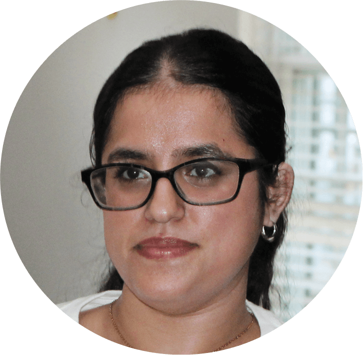 A woman with dark hair pulled back, wearing glasses and small hoop earrings, looks slightly off camera with a neutral expression. She is indoors, in front of a window with blinds, reviewing the AHC Impact Report 2024.