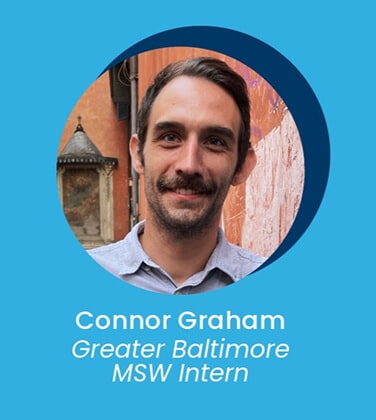 A man with short brown hair and a mustache smiles at the camera, standing outside against a colorful wall. Text below reads: Connor Graham, Greater Baltimore MSW Intern.