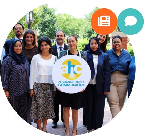 A diverse group of people smiling outdoors, with one person holding a round sign that reads “AHC Affordable Homes & Communities,” representing the spirit of Affordable Homes & Communities. Two colorful icons are in the upper right corner.