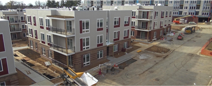 New affordable homes and communities are taking shape, with new apartment buildings under construction, unfinished landscaping, and construction equipment on a paved road surrounded by more projects in progress.
