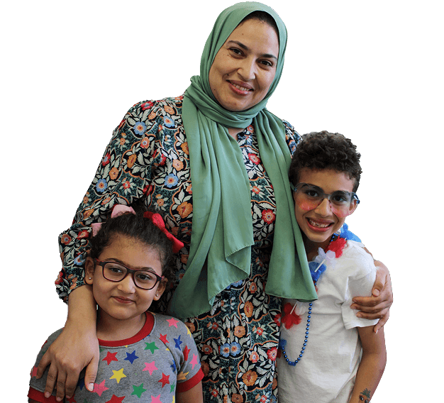 A smiling woman in a green headscarf and floral dress stands with her arms around two smiling children, embodying the warmth and togetherness found in Affordable Homes & Communities.