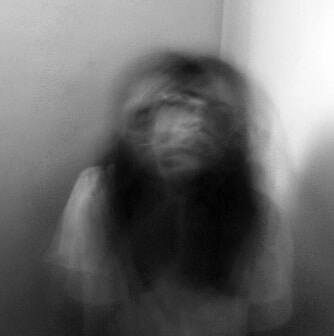 A blurry, black-and-white photo of a person with long hair sitting against a wall, their face and head motion-blurred for a ghostly effect—Gold Key Winner: CCR Student Tells Mental Health Story Through Art.