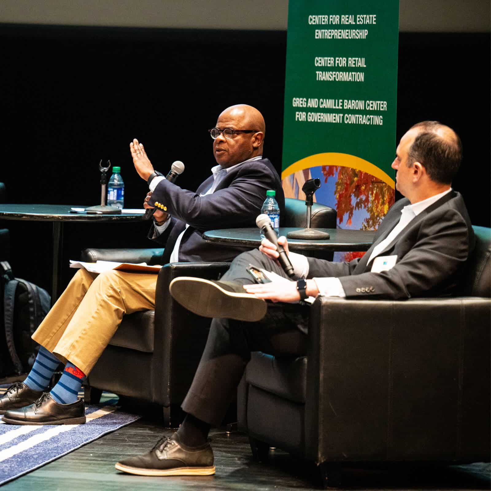 two men talking during an interview on the stage about investing
