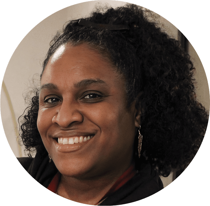 A woman with curly black hair, wearing earrings and a black top, smiles warmly at the camera. The softly blurred background hints at a professional setting, perfect for the AHC Impact Report 2024.