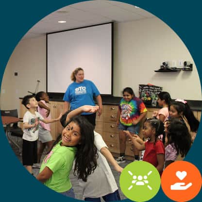 A group of children happily play and dance indoors with a smiling adult, highlighting Resident Services supervision. The background shows a screen and cabinets. Two icons, a sun and a heart in hands, appear at the bottom.