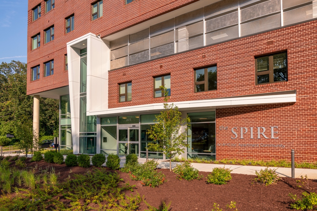 A modern brick building with large windows and a glass entrance labeled SPIRE and UMass Amherst Commonwealth Honors College, surrounded by landscaped greenery.